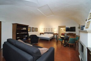 A living room with a sofa, a bed, a dining table with chairs, a bookshelf, and a TV.