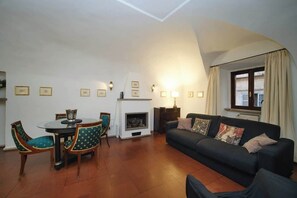 A living room with a fireplace, a sofa, a dining table with chairs, and framed pictures on the wall.