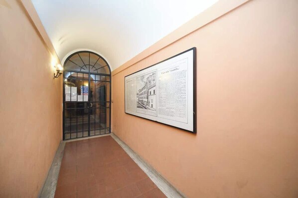 A corridor with a framed historical document on the wall, a metal gate, and a wall-mounted light fixture.
