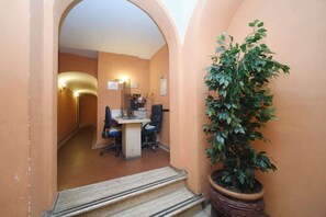 A hallway with a desk and chairs, a potted plant, and an archway.
