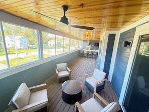 Un espacio al aire libre techado con piso de madera, ventilador de techo y un conjunto de mesasillas con sillas y una mesa redonda.