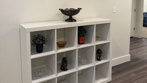 Un couloir avec une console blanche, un tableau représentant un paysage urbain et une plante en pot.