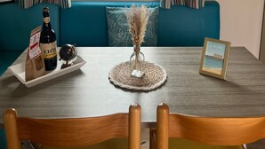 Uma sala de jantar com mesa, cadeiras, uma garrafa de vinho, um tabuleiro, um vaso decorativo e um quadro emoldurado.