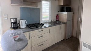 Uma cozinha compacta com fogão a gás, chaleira, micro-ondas e geladeira.