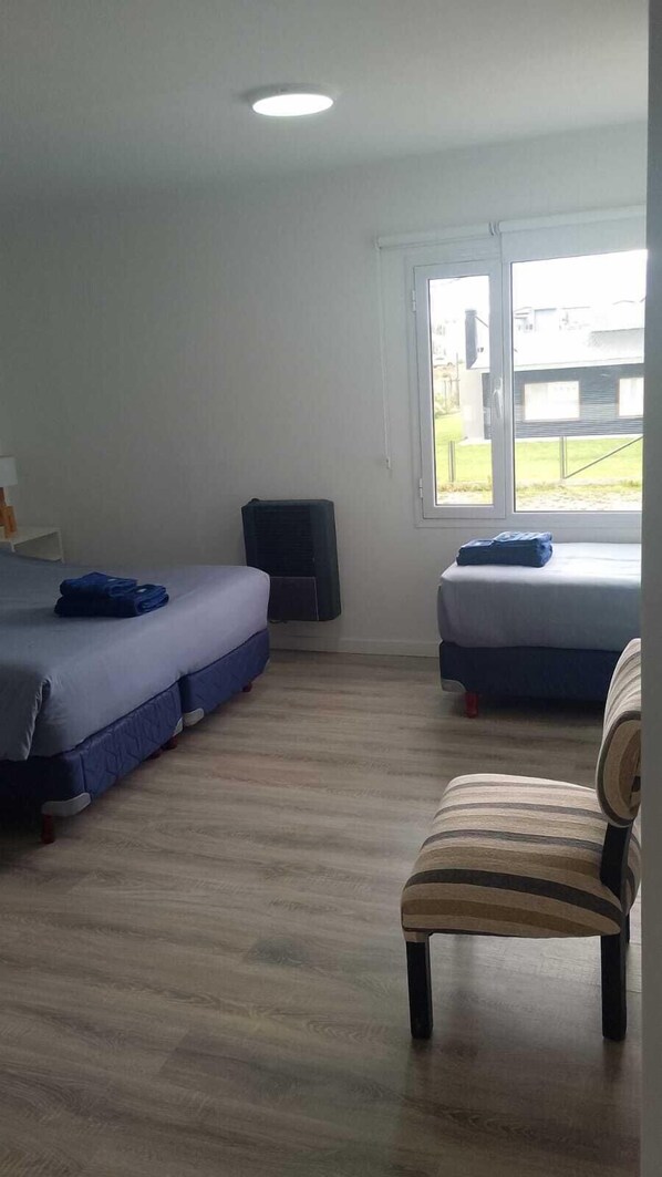 A room with two beds, a window, a chair, and a ceiling light. - Adventure Aparts (El Calafate)