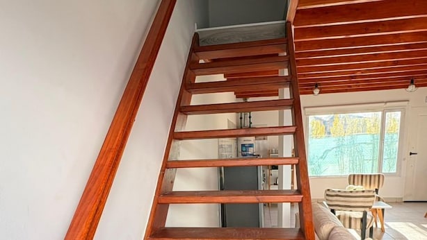 Un escalier en bois, doté d’une rampe, mène à une pièce où se trouvent un canapé et une fenêtre.
