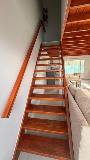 A wooden staircase with a handrail, leading to a room with a sofa and a window. - Adventure Aparts (El Calafate)
