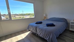 Une chambre à coucher avec un lit, deux tables de chevet, une fenêtre et une vue sur l’extérieur.