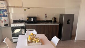 Une cuisine moderne avec une table blanche, deux chaises blanches, une cuisinière, un four et un réfrigérateur.