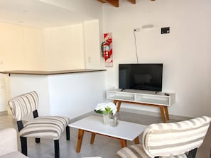 A modern living room with a flat-screen TV, two striped armchairs, a white coffee table, and a small vase with flowers. - Adventure Aparts  (El Calafate)