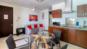 A modern kitchen with a microwave, stove, and cabinets. There is a dining area with a glass table and chairs. - Walk to the beach from your luxury living apartment (Playa del Carmen)