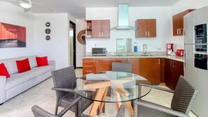 A modern kitchen with wooden cabinets, a glass dining table, and a white sofa with red cushions. - Walk to the beach from your luxury living apartment (Playa del Carmen)