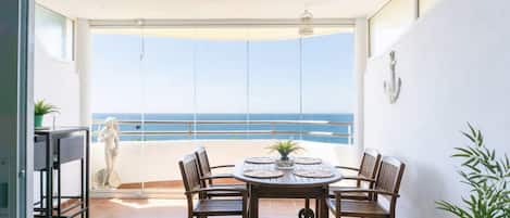 A balcony with a table and chairs, a statue, and a view of the ocean.