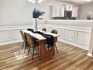 A modern kitchen with white cabinetry, a central island, and a dining area with a wooden table and chairs. - Game House - Hot Tub - Sleeps 10 (Atlanta)