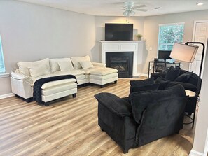 A living room with a sectional sofa, a loveseat, a black armchair, a fireplace, and a ceiling fan. - Game House - Hot Tub - Sleeps 10 (Atlanta)