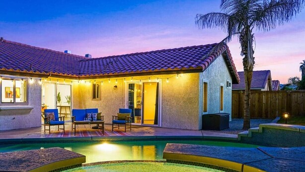 Une maison avec une piscine, du mobilier de jardin et un palmier.