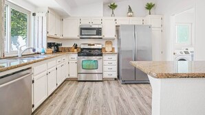 Une cuisine moderne avec des armoires blanches, des appareils en acier inoxydable, des comptoirs en granit et un plancher en bois.