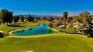 Un parcours de golf avec un étang central, entouré de pelouses et d’arbres bien entretenus.