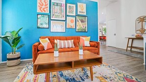 Un salon avec un mur d’accent bleu, une table basse en bois, un canapé orange et divers tableaux encadrés.