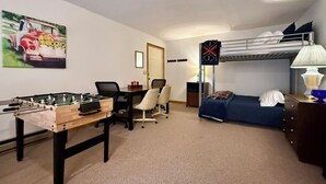 Una habitació amb taula de futbolí, llit superposat, escriptori amb cadira i sofà.