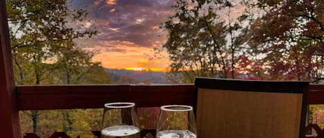 Dos copas de vino blanco sobre una mesa con vistas a una puesta de sol y árboles.