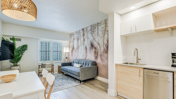 A modern kitchen with a dishwasher, a dining area with a white table and chairs, and a grey sofa.