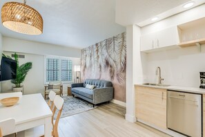 A modern kitchen with a dishwasher, a dining area with a white table and chairs, and a grey sofa. - Condo near Epic & Universal, free parking+Netflix (Orlando)