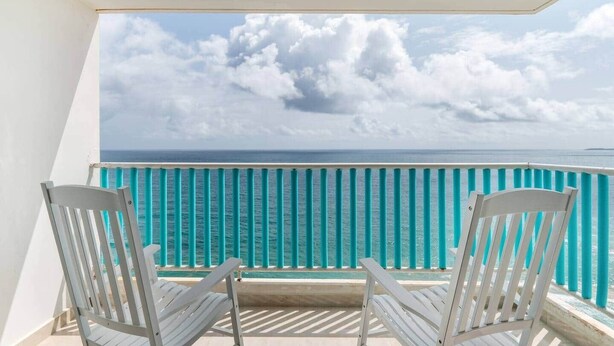 A balcony with two white chairs, a turquoise railing, and a view of the ocean.