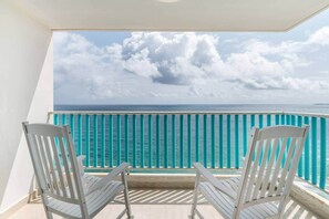 Een balkon met twee witte stoelen, een turquoise reling en uitzicht op de oceaan.