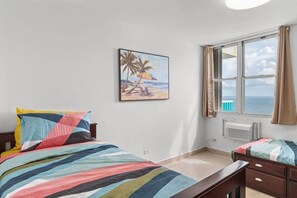 Un dormitorio con cama, mesita de noche, ventana con vista al mar y un cuadro en la pared.