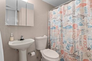Un baño con lavamanos blanco, inodoro y cortina de ducha con diseños marinos.