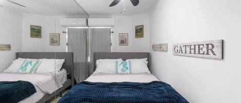 Una camera d'albergo con due letti, una ventola a soffitto e un cartello con la scritta 'GATHER'.