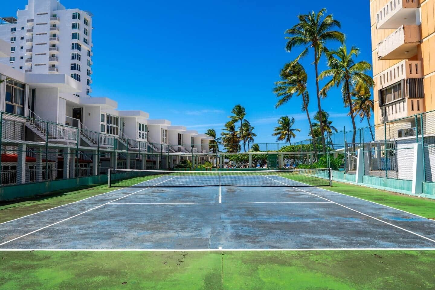 Una cancha de tenis con edificios circundantes y palmeras.
