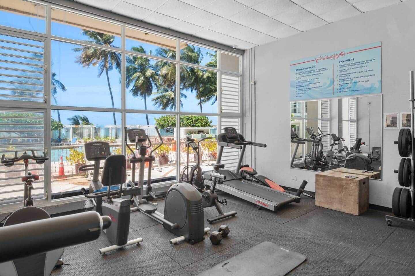 Un gimnasio con máquinas de cardio, pesas libres y un espejo grande.