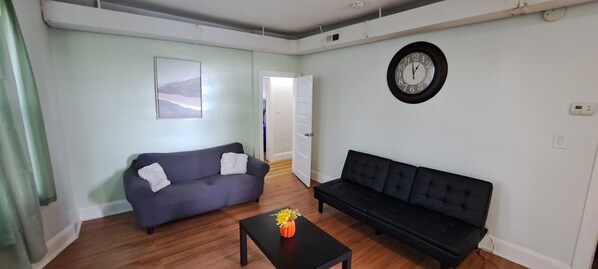 A living room with a grey sofa, a black sofa, a coffee table with a vase, and a clock on the wall.