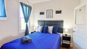 A bedroom with a large bed, a headboard, a nightstand, a lamp, and a door. - Historic Charm W/ Modern Patio Escape (Baltimore)