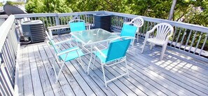 Une terrasse dotée d’une table à plateau en verre et de chaises bleues, entourée d’une rambarde blanche.