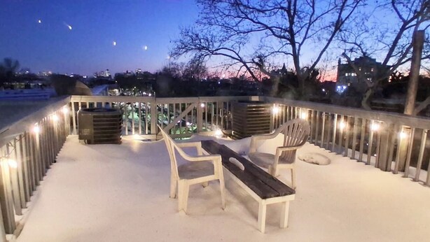 A snow-covered deck with a wooden bench and chairs, surrounded by a railing with lights. - Historic Charm W/ Modern Patio Escape (Baltimore)