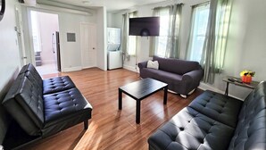 A living room with a sofa, a coffee table, and a TV mounted on the wall. - Historic Charm W/ Modern Patio Escape (Baltimore)