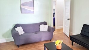 A living room with a grey sofa, a black sofa, and a coffee table with a vase of flowers. - Historic Charm W/ Modern Patio Escape (Baltimore)