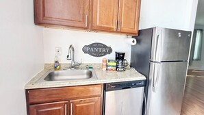 A kitchen with wooden cabinets, a stainless steel refrigerator, a dishwasher, and a coffee maker on the counter. - Historic Charm W/ Modern Patio Escape (Baltimore)