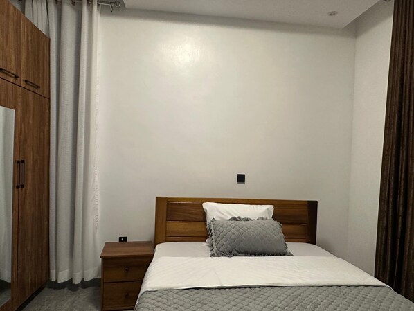 Un dormitorio con estructura de cama de madera, colchón blanco y manta acolchada gris.