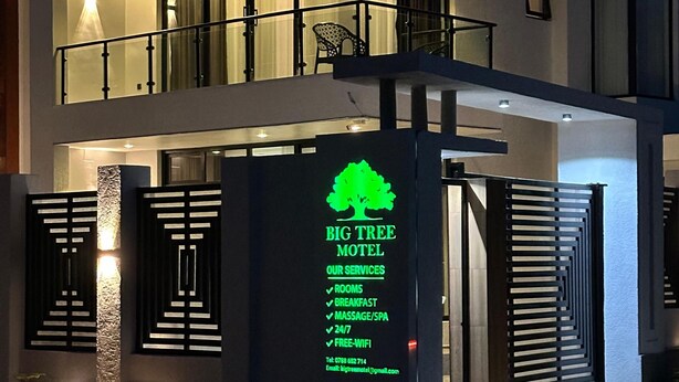 A modern two-story motel with a prominent sign listing services like rooms, breakfast, massage, 24/7 availability, and free WiFi. - BIG TREE MOTEL (Ruhengeri)