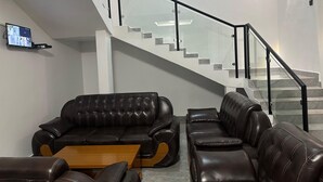 A modern living room with a leather sofa set, a wooden coffee table, and a staircase with glass railings. - BIG TREE MOTEL (Ruhengeri)