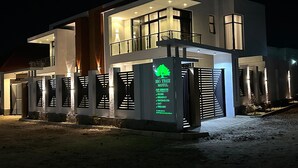 A modern two-story motel with a prominent signboard listing services like rooms, breakfast, massage/SPA, and free WiFi. - BIG TREE MOTEL (Ruhengeri)