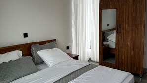 A modern bedroom with a large bed, wooden wardrobe, and a mirror. - BIG TREE MOTEL (Ruhengeri)