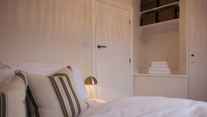 A neatly made bed with pillows, a bedside lamp, and a white wardrobe with baskets. - Beautifully Refurbished Terrace – Just a 15-Minute Riverside Walk into York (York)