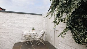 A small outdoor seating area with a round table and two chairs, a potted plant, and a white brick wall. - Beautifully Refurbished Terrace – Just a 15-Minute Riverside Walk into York (York)