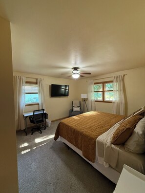 A bedroom with a bed, a desk, a chair, a TV, and a ceiling fan. - Par-fect Escape on Lake Windsor Golf Course (Windsor)