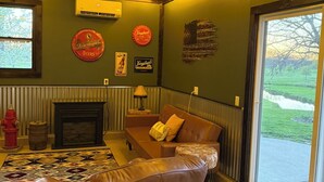A cozy living room with a brown leather sofa, a fireplace, a large window with a view of a green landscape, and wall decorations including beer bottle caps and a sign. - Par-fect Escape on Lake Windsor Golf Course (Windsor)